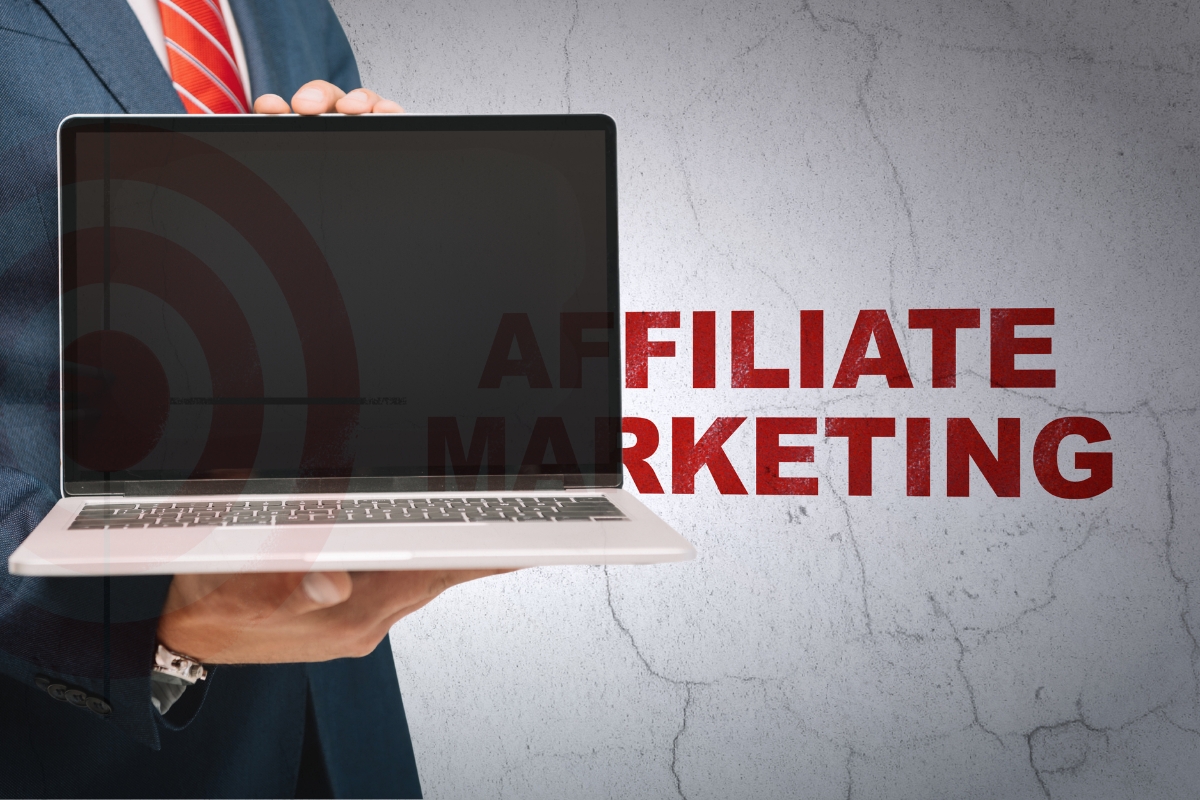 osoba u odelu drži laptop u ruci u pozadini zid na kom piše affiliate marketinga